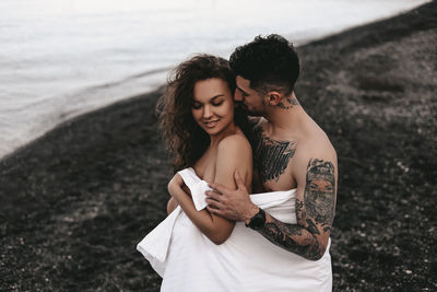 A couple in love spend the night at the sea, kissing and hugging on the beach covered with a blanket