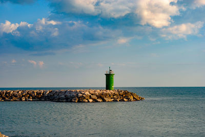 Lighthouse by sea against sky during sunset