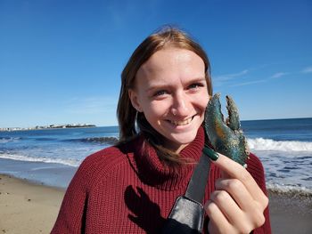 Portrait of smiling woman holding claw at beach against sky