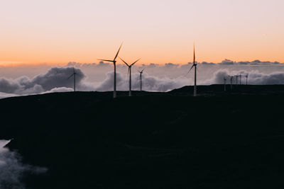 Silhouette of wind turbines against sky during sunset