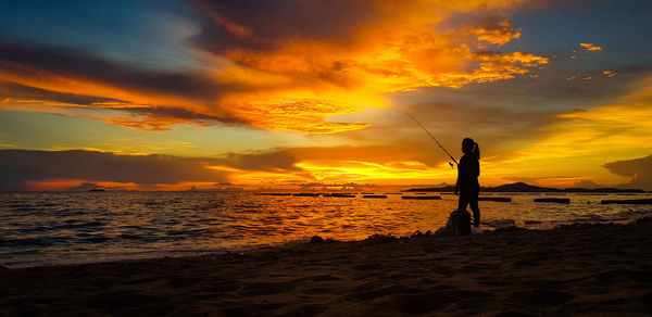 Silhouette woman fishing at beach against sky during sunset
