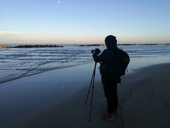 Rear view of photographer standing at beach against sky