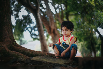 Cute boy sitting on tree roots in park