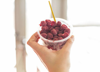Cropped image of person hand holding disposable cup filled with raspberries