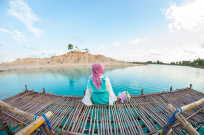 Woman sitting on pier over lake against sky