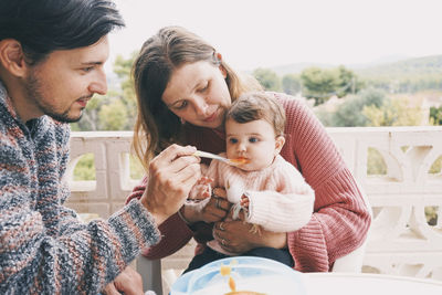 Man and woman feeding baby girl in balcony