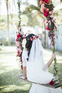 Rear view of bride wearing wedding dress with flowers and veil outdoors