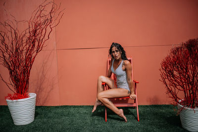 Woman sitting on chair against plants against wall