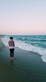 Rear view of woman standing on shore at beach against sky