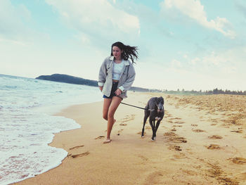 Teenage girl with dog running at beach