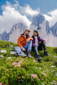 Full length of friends sitting on mountain against sky