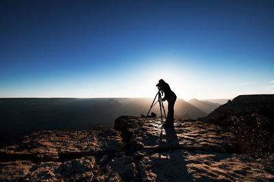Man photographing on rock against clear sky