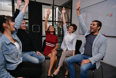 Happy colleagues with hand raised sitting on chairs in board room