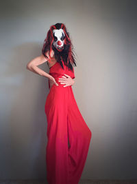 Woman standing dressed in red wearing scary clown mask