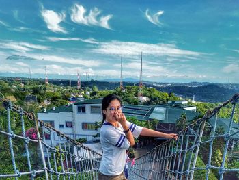 Portrait of smiling woman standing on footbridge against sky