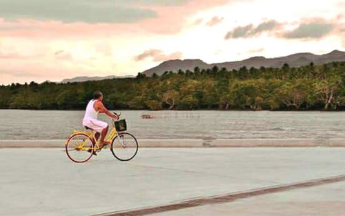 Woman cycling on bicycle by lake against sky