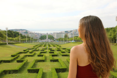 Rear view of woman standing at ornamental garden against cloudy sky