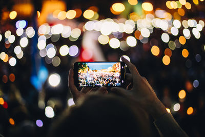 Midsection of person photographing illuminated mobile phone at night