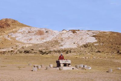 Woman sitting on landscape against clear sky