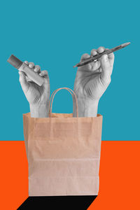 Cropped hand of woman holding shopping bag against blue background