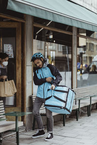 Delivery man collecting order from female owner at delicatessen shop during pandemic