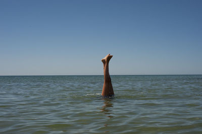 Woman swimming with feet up in sea against clear blue sky