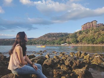 Woman sitting on rock by lake against sky