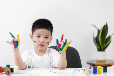 Portrait of boy holding paper against colored pencils on table