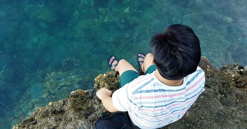 High angle view of man sitting on rock by sea