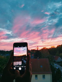 Hand holding smart phone against sky during sunset