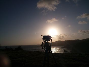 Silhouette man photographing sea against sky during sunset