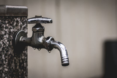 Close-up of wet metallic faucet attached on wall