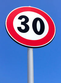 Low angle view of road sign against clear blue sky