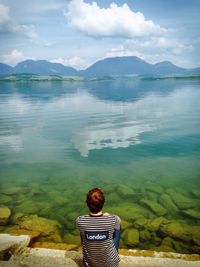 Rear view of man sitting against lake