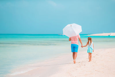 Rear view of father and daughter walking on beach