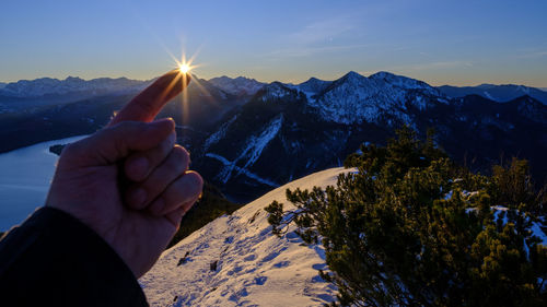 Person hand on snowcapped mountain against sky during winter