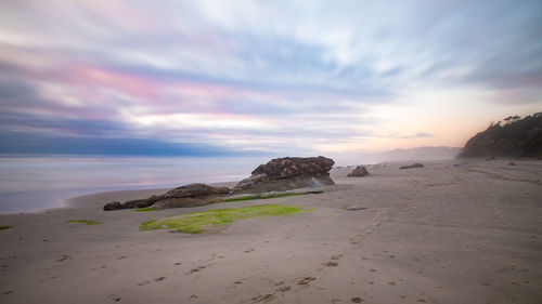 Rocks on beach against sky during sunset