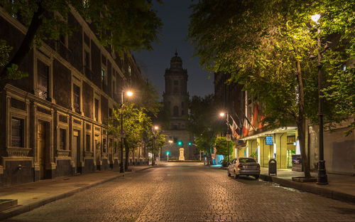 Illuminated road amidst buildings leading towards metropolitan cathedral at night