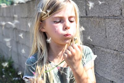 Close-up of girl blowing dandelion on field