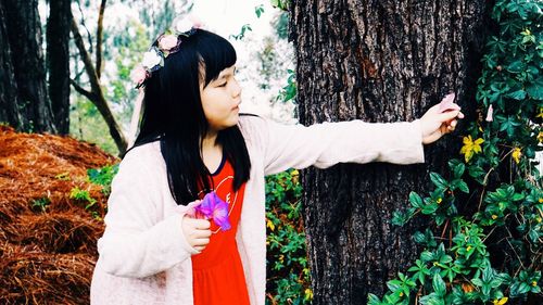 Girl plucking flowers from plant by tree trunk