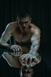 Shirtless man with tattoo sitting at table against black background