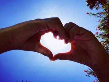 Cropped hands of woman making heart shape against sky during sunny day