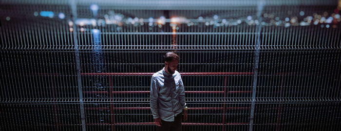 Panoramic view of man standing against metallic fence at night