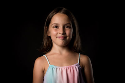 Portrait of smiling girl standing against black background