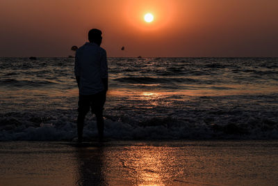 Rear view of man standing on beach during sunset