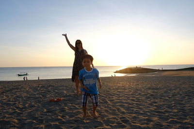 Woman standing on beach against sky during sunset