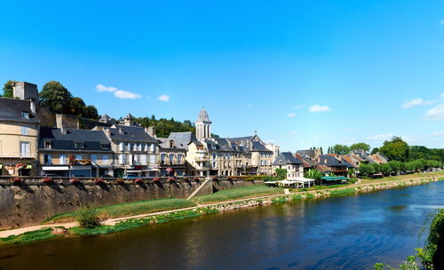 Houses by river and buildings against blue sky