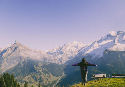 Rear view of woman with arms outstretched standing against snowcapped mountains