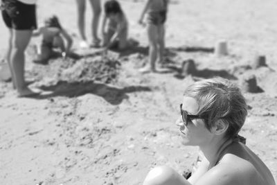 Side view of thoughtful woman wearing sunglasses looking away while sitting at beach during sunny day