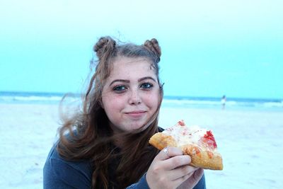 Portrait of teenage girl eating pizza at beach against sky